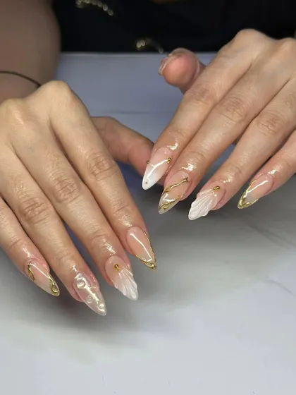 An elegant design with a mix of textures. These stiletto nails feature a nude base with gold chrome tips and delicate, sculpted 3D shell accents.