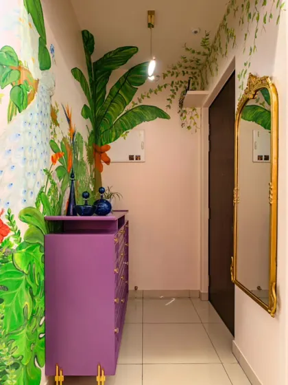 A wider view of the foyer, where the tropical mural extends along the corridor, complemented by a vintage-style gold mirror that adds a touch of classic elegance.