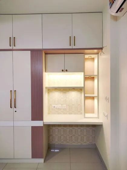 A bedroom from the Divinity Home featuring a wardrobe and integrated study nook in a soft pink and white palette with gold accents, creating a space that is both elegant and functional.