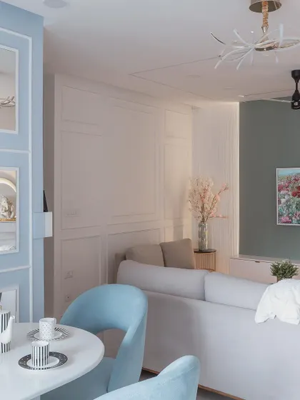 This living room uses a soft pastel blue and white color palette for a calm and airy feel. The curved blue chairs and modern ceiling fan add a touch of contemporary style.