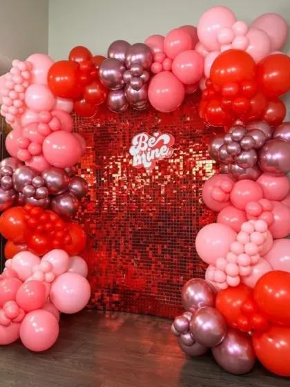 For a touch of glam, this Valentine's setup includes a shimmering red sequin wall. It's framed by a garland of red and pink balloons with a "Be Mine" sign, perfect for a fun party.