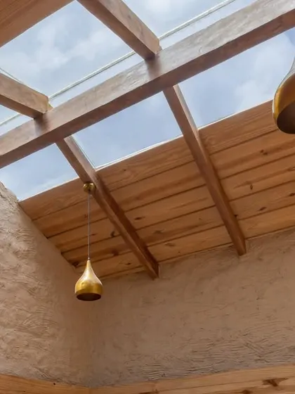A new skylight floods the interior with natural light, illuminating the wooden ceiling beams, brass pendant lights, and the tactile texture of the walls.