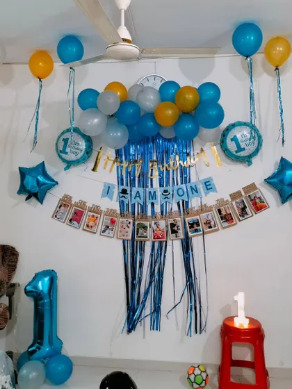 A classic first birthday home setup with a blue fringe curtain, photo banner, and blue and yellow balloons.