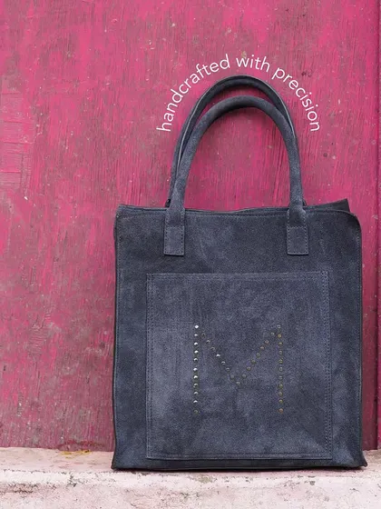 A spacious and sturdy suede tote, ideal for your travel needs. This version in grey suede features a hand-studded 'M' pattern for a subtle branding touch.