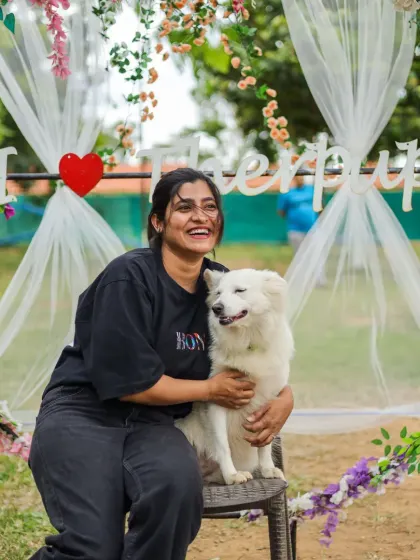 All smiles at the Barkday Bash! A pet parent shares a happy moment with her beautiful white dog at our floral photo booth.