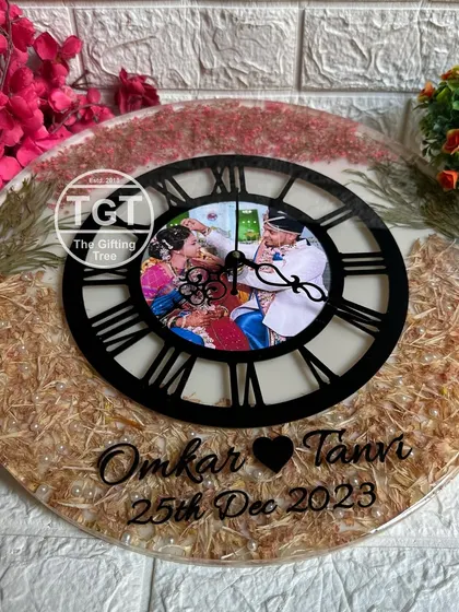 A straight-on shot of the 16-inch memory clock, showing the couple's names and wedding date inscribed at the bottom. The design balances preserved flowers with clear space.