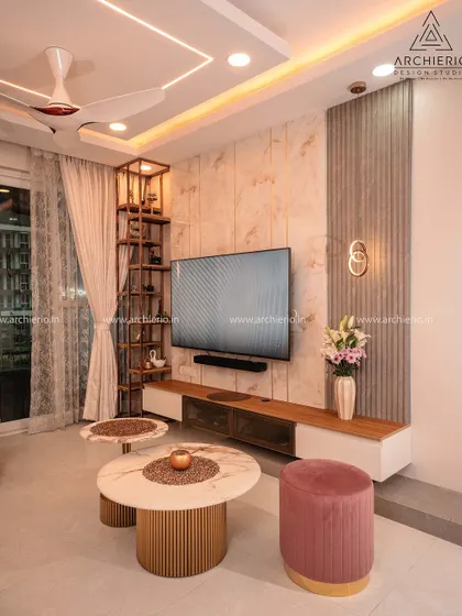 A living room with a sophisticated TV unit, featuring a combination of marble and fluted wood panels, and a comfortable pink ottoman for a pop of color.
