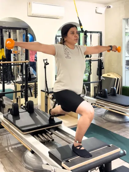 Strong, focused, and in control. This client performs a lunge on the moving Reformer carriage while holding weights, a compound exercise that builds full body strength.