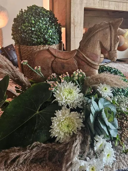 A close-up of a centerpiece from a teddy bear-themed baby shower, featuring a wooden rocking horse and a beautiful arrangement of white flowers and pampas grass.