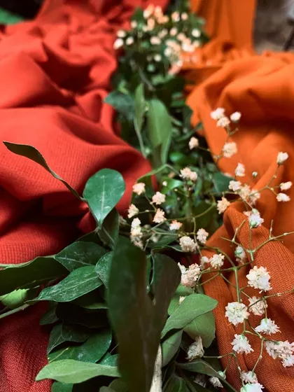 A close-up of the textured orange and red fabrics, accented with a simple line of greenery and baby's breath. This shows our attention to detail in layering materials.