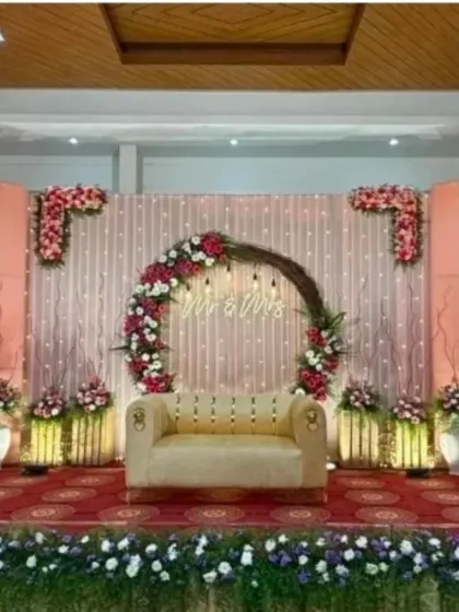 A beautiful engagement stage with a rustic twig arch decorated with pink and white flowers and a 'Mr & Mrs' neon sign.