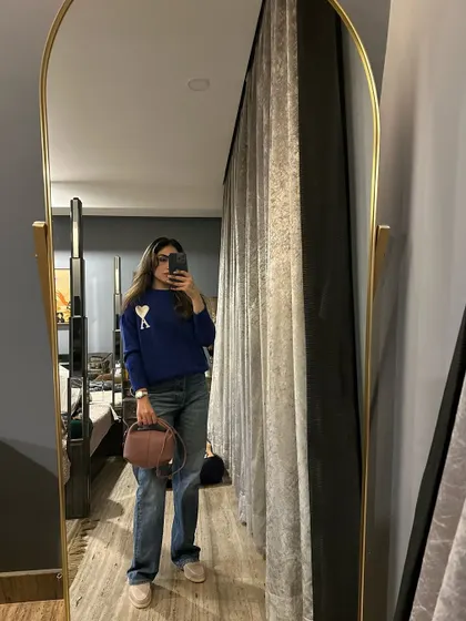 A casual winter look with a blue sweater, jeans, and a pink bag.