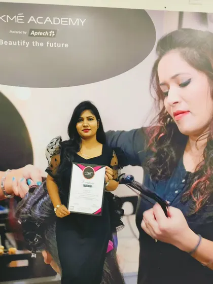 A full-length shot of a student on her graduation day, standing in front of the Lakme Academy branding. This represents the culmination of her hard work and training.