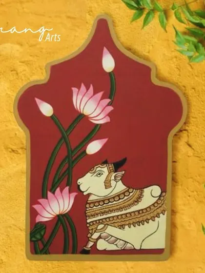 This hand-painted wall hanging features a Pichwai cow amidst lotuses, a classic theme symbolizing purity and devotion. The unique shape and artistic style make it a standout piece of decor.