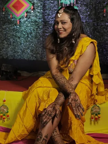 A happy bride posing for a photo during her mehandi ceremony, showcasing the full hand and leg designs I created for her.