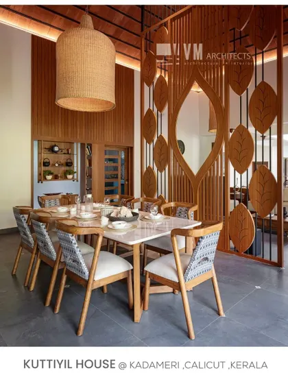 The dining area at Kuttiyil House features a classy marble table and chairs with traditional fabric, all under a large woven pendant light that adds warmth and texture.