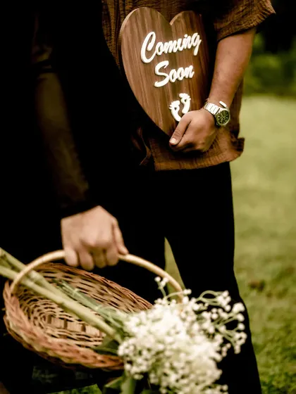A detail shot focusing on the props of the journey: a basket of flowers and the "Coming Soon" sign, held by the couple.