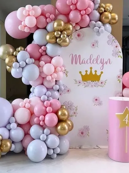 A sweet princess-themed party for a 4th birthday. The decoration features a pink, purple, and gold balloon arch over a custom backdrop with a crown motif.