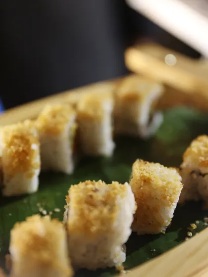 A close-up of our crispy sushi rolls, presented on a banana leaf. The toasted crumb topping adds a delightful textural contrast to the soft rice and filling.