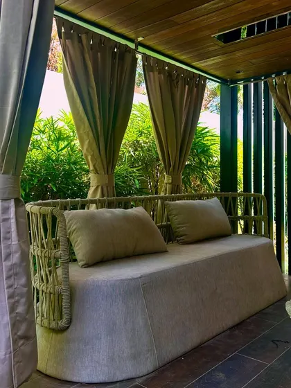 A detail shot of the plush sofa and curtains. The fabric's neutral tones complement the natural colors of the wood, stone, and surrounding plants.