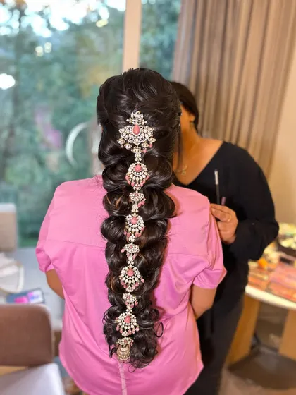 The finished hairstyle for the Varapooja. This is a modern take on a traditional braid, using stunning pink and white stone-studded accessories instead of fresh flowers.