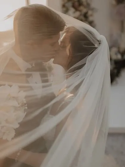 A beautiful, intimate moment under the veil, as the Christian couple shares a kiss after their vows. The golden light adds a dreamy feel.