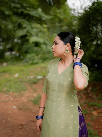 A portrait of actress Anupama Gowda in a simple green kurta, set against a natural background. Her pose and expression convey a sense of calm and grace.