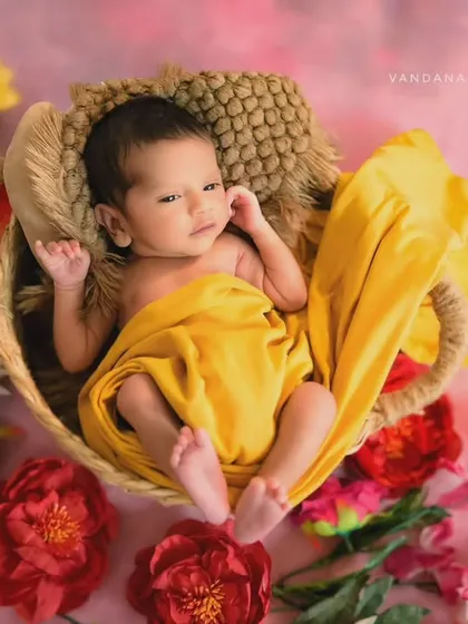 This newborn portrait is filled with warmth and color. The baby is nestled in a soft basket, draped in a bright yellow cloth and surrounded by vibrant flowers, creating a cheerful 'Little Miss Sunshine' theme.