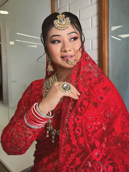 A close-up portrait of the bride in the red saree, highlighting her jewellery and radiant smile.