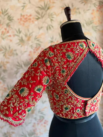 This red bridal blouse features a classic round keyhole back, bordered with heavy zardozi embroidery that matches the work on the sleeves.