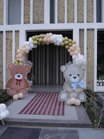 The entrance to the baby shower, framed by a balloon arch and two large, welcoming teddy bear cutouts.