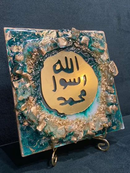 This is a small, square tabletop piece featuring the Mohr e Nabuwat. The gold mirror calligraphy is set against a rich emerald green resin, with a textured border of gold leaf and crystals.