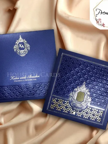 A royal blue premium invitation with intricate silver and gold embossed patterns and a custom monogram, exuding luxury and sophistication.
