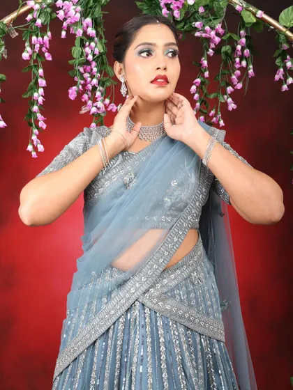 The model posing in a beautiful grey-blue lehenga. The makeup is designed to complement the cool tones of the outfit.