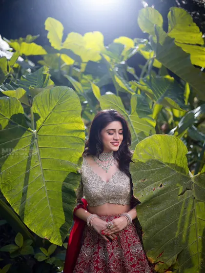 Mahima smiling, surrounded by lush greenery. Her makeup is light and radiant, perfect for a daytime event or an outdoor photoshoot.