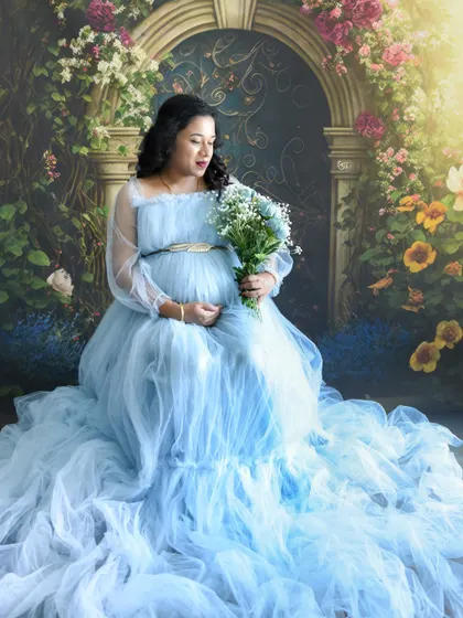 A dreamy, seated portrait of a mom-to-be in a light blue gown, holding flowers in our floral studio.