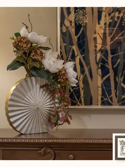 This stunning floral arrangement in a unique fan-shaped vase adds a touch of modern artistry and sophistication to this classic wooden chest of drawers.