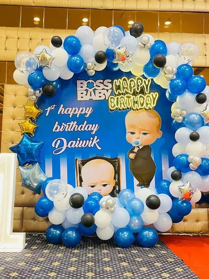 A grand "Boss Baby" themed first birthday party. The centerpiece is a large circular backdrop with characters, framed by a blue, white, and black balloon arrangement.