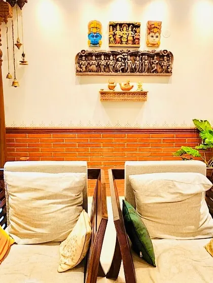 A seating area with traditional wooden chairs, carved pillars, and a wall adorned with ethnic masks and carvings.