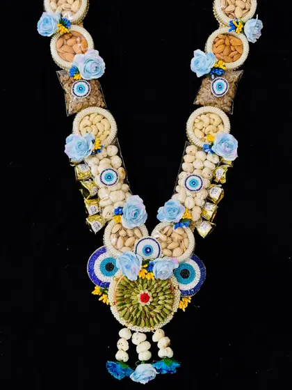 This beautiful dry fruit garland is decorated with blue flowers and evil eye beads for a touch of elegance and protection. It’s a thoughtful and healthy gift for your loved ones this Holi.