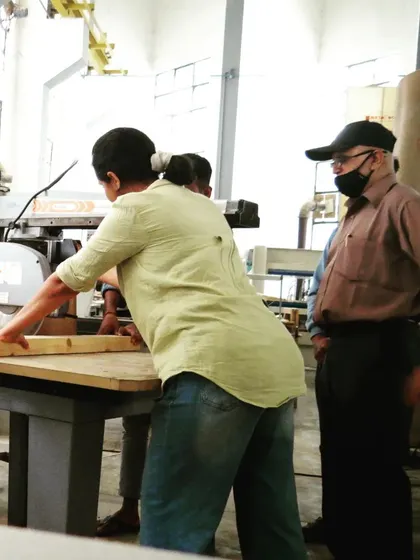 An instructor supervises as a student makes a cut on a large piece of timber, ensuring proper technique and safety at all times.