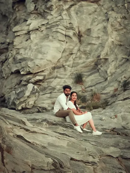 A wide-angle pre-wedding shot of a couple sitting together against a vast, rocky landscape, highlighting the scale of nature.