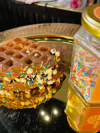 A close-up of a waffle topped with chocolate and colorful sprinkles.