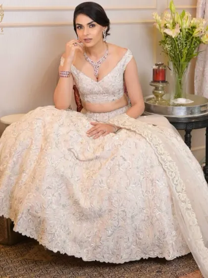 A vision in white. The bride is seated, showcasing her full lehenga and the stunning ruby and diamond necklace that adds a pop of colour to her look.