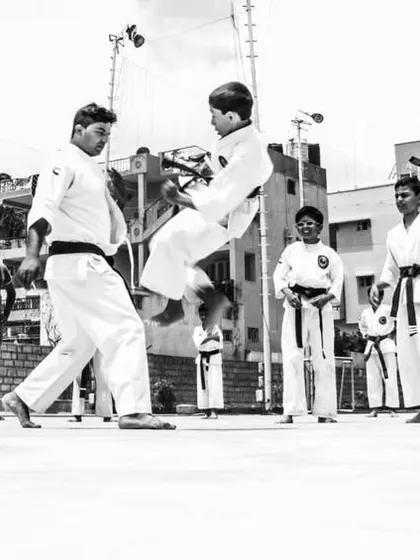 A black and white action shot of a flying kick demonstration, showing the dynamic and athletic side of karate.