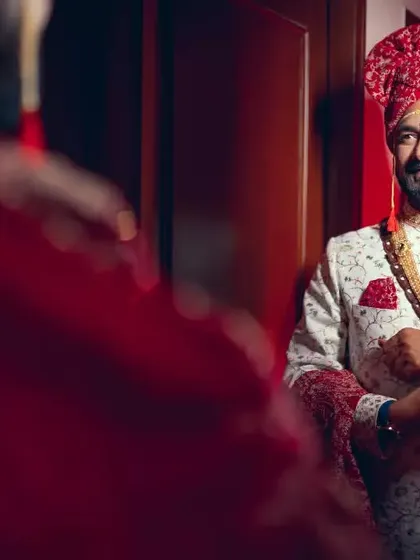 The groom looks at his reflection in the mirror, adjusting his attire, ready for the big moment.