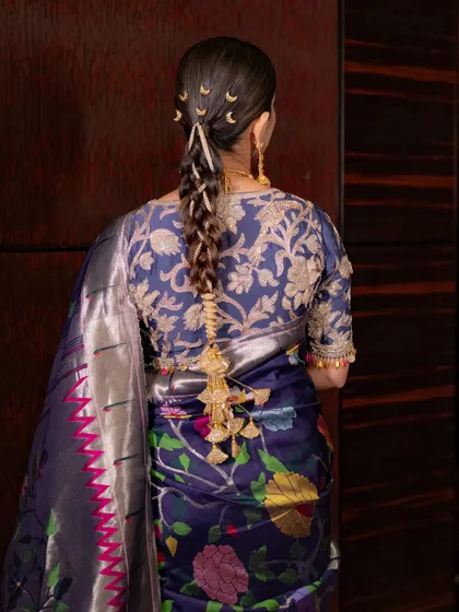 The hairstyle is a work of art. This sleek choti is adorned with classic Maharashtrian hair accessories, including the crescent moon clips, adding a touch of redefined elegance.