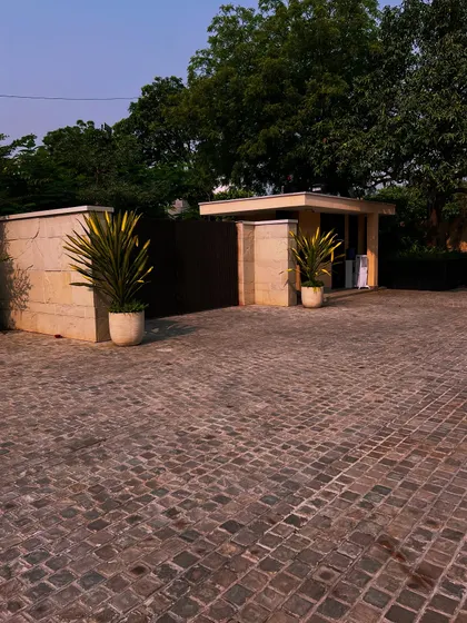 A view of the cobblestone driveway and security gatehouse, framed by mature trees. The hardscaping and softscaping work together to create a cohesive and impressive entry experience.
