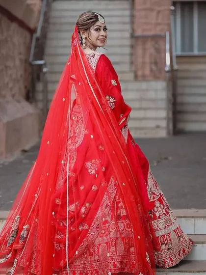 A full-length view showcasing how the complete look comes together. The vibrant red lehenga is balanced with makeup that is elegant and defined, creating a cohesive and regal bridal appearance.