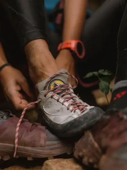 Lacing up climbing shoes over hiking shoes. This shot shows the transition from the approach to the climb, a key part of the outdoor climbing ritual.